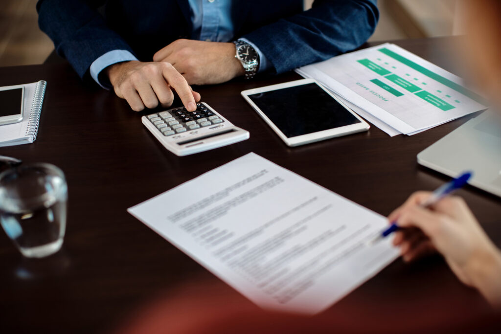 Close-up of real estate agent using calculator while his client